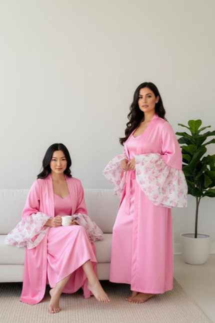 Two women in pink intentional soft mom satin robes with lace cuffs sitting on a couch.